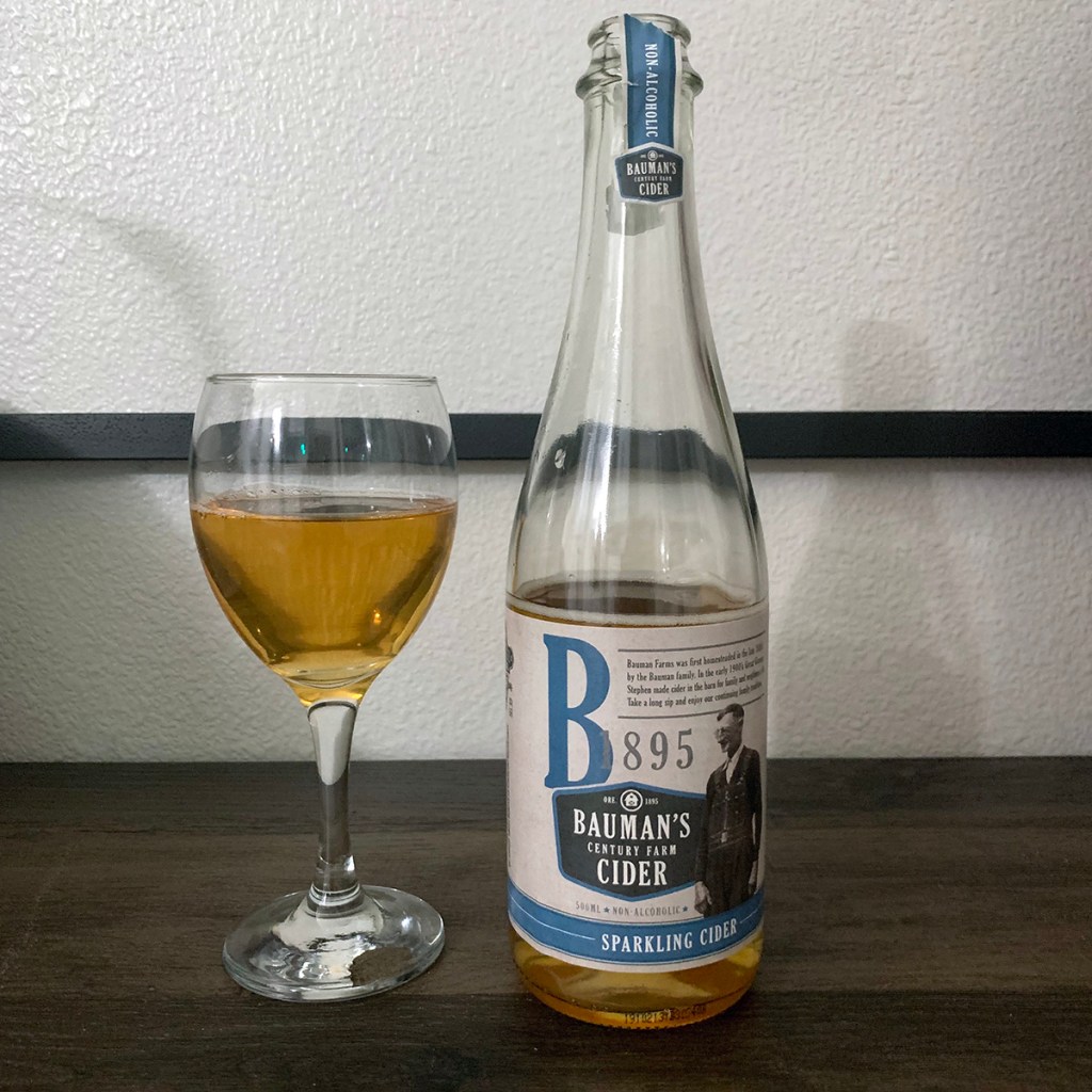 A glass of cider sits next to a bottle of sparkling cider from Bauman's Cider