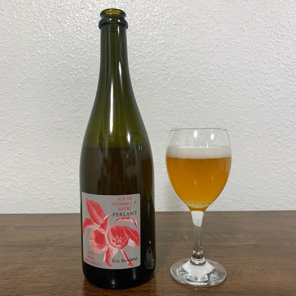 A glass of cider sits next to a bottle of Perlant from Eric Bordelet cider