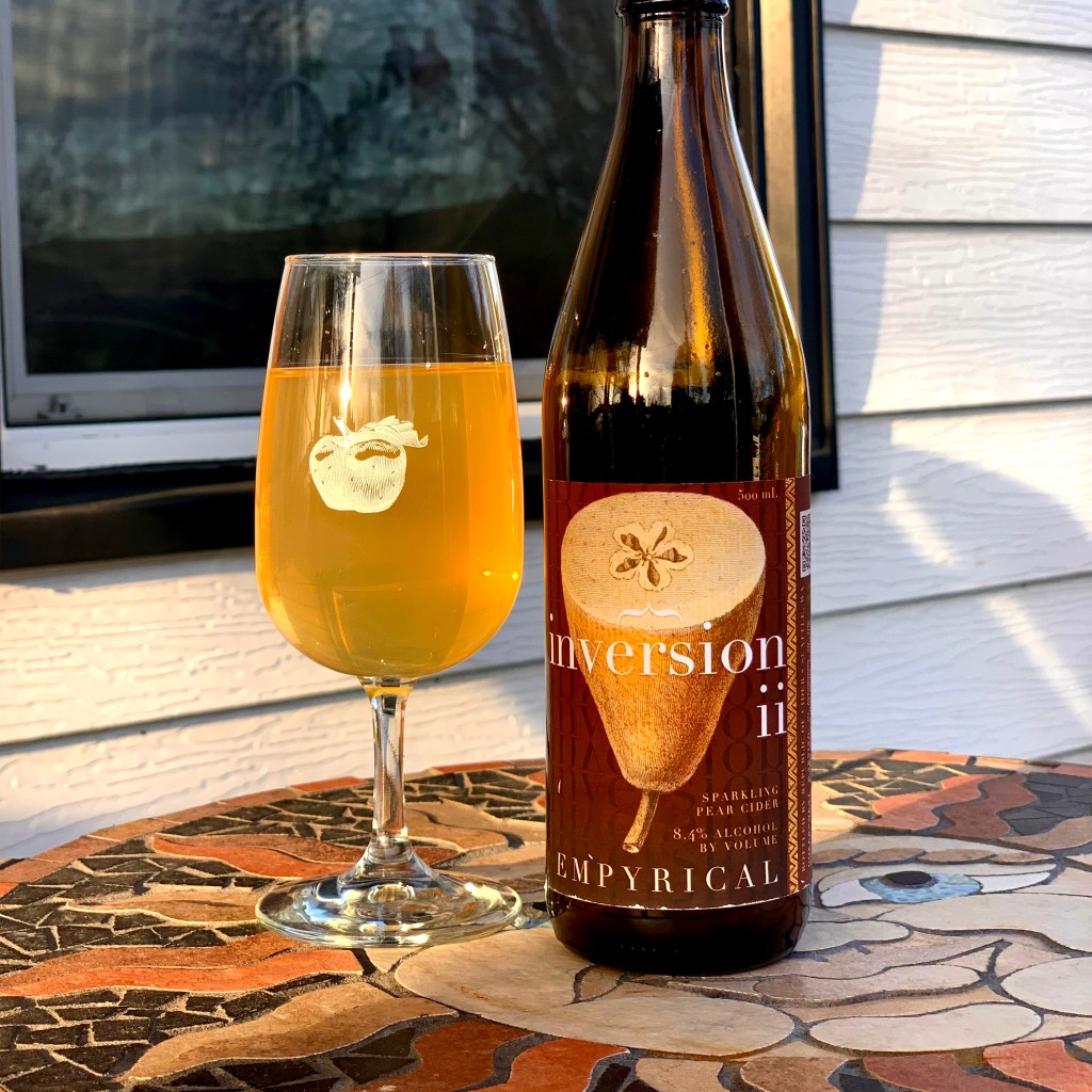 A glass of cider sits on a mosaic table next to a bottle of Inversion II from Empyrical Cider