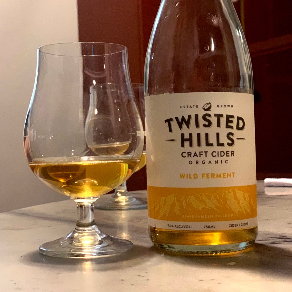 A glass of cider next to a bottle of Wild Ferment by Twisted Hills Craft Cider